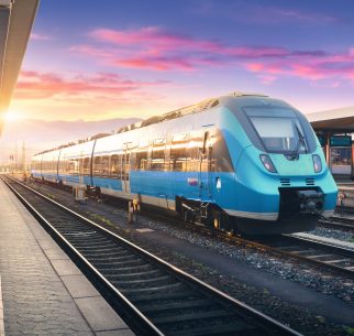 A bright blue modern train sits at the station with tracks leading off into the distance
